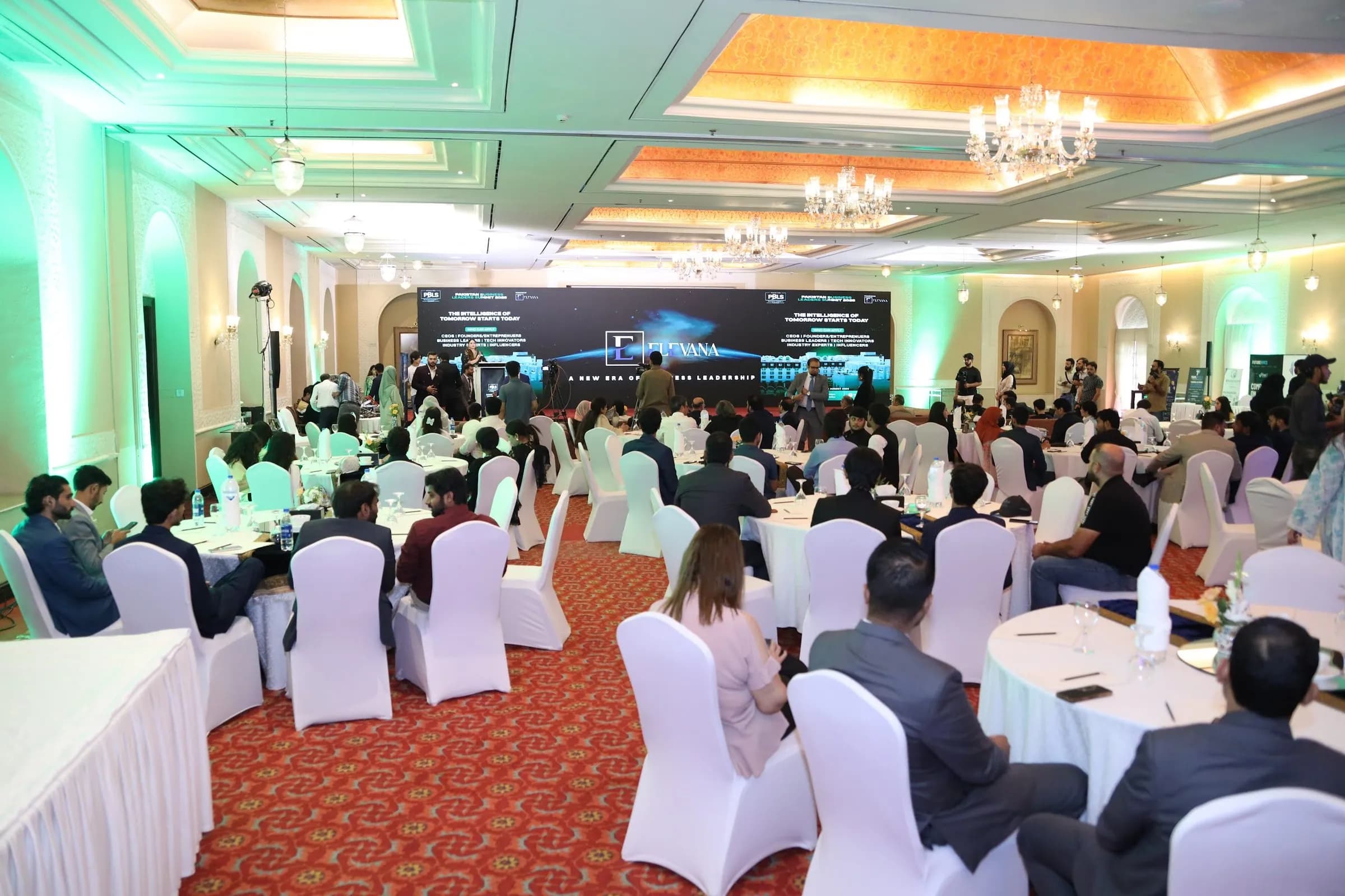 The ballroom filled with delegates at round tables under green stage lighting at PBLS Serena Islamabad